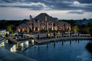 A waterside mansion is lit up at night with beautiful landscaping