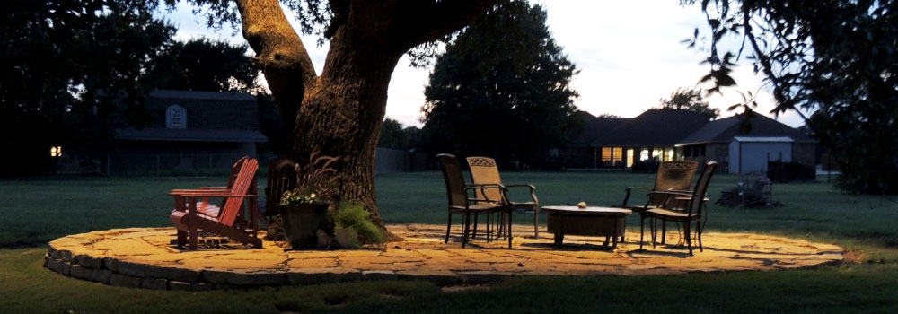 Lighted tree and patio furniture on stone slab in backyard