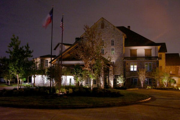 Landscape lighting surrounding a house with two flag poles and a circular driveway