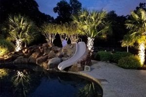 pool with rock waterfall and slide with trees lit up with outdoor lighting