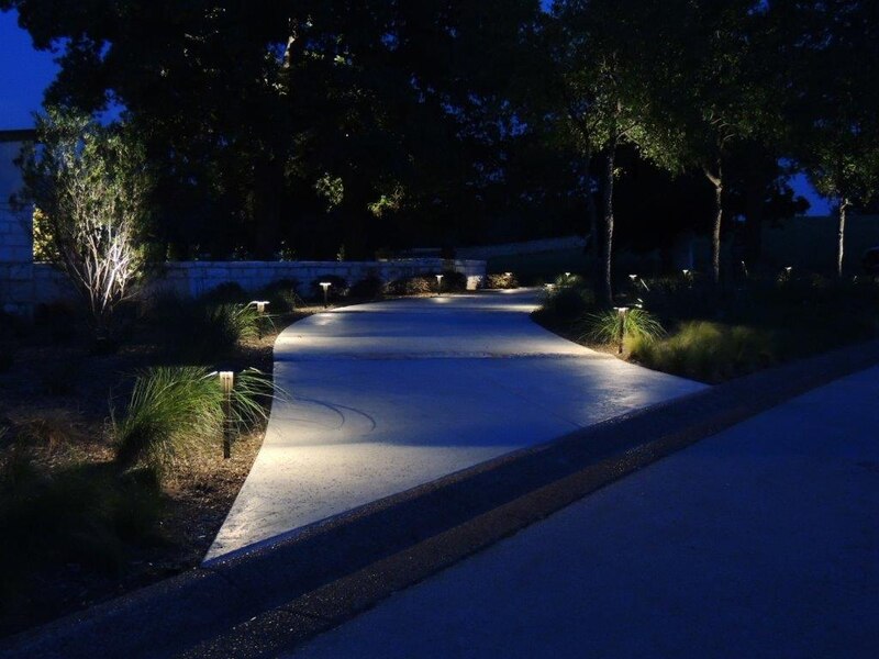 drive way lined with trees lit up with outdoor lighting