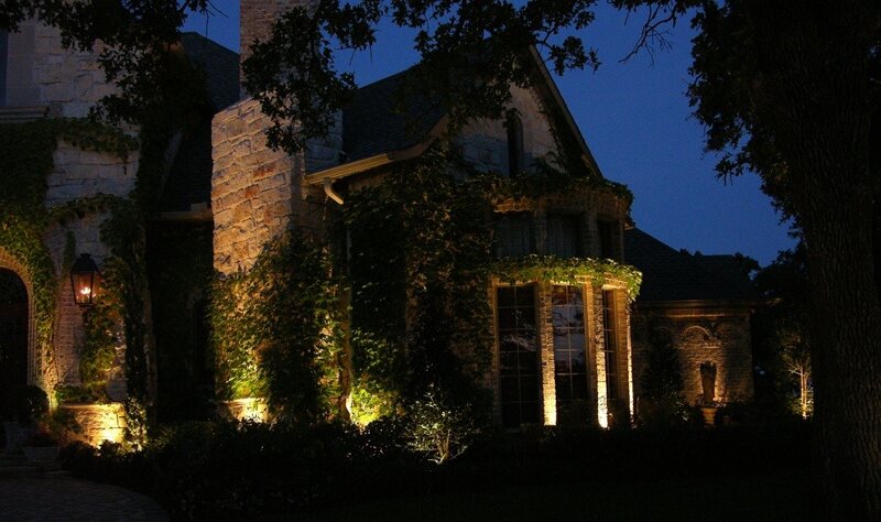 a home covered in vines being lit up with outdoor lighting